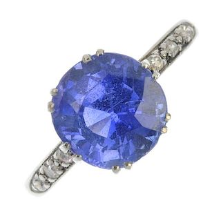 A sapphire and diamond ring. The circular-shape sapphire, with single-cut diamond line shoulders, to