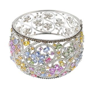 A diamond and sapphire hinged bangle. Designed as a series of vari-colour sapphire floral clusters,