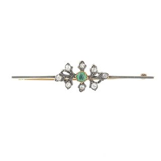 An emerald and diamond brooch. The circular-shape emerald, within an old-cut diamond foliate surroun