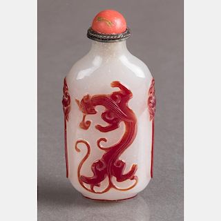 A Red-Cut-to-White Peking Glass Snuff Bottle with Coral and Silver Stopper on a Carved Hardwood Stand.