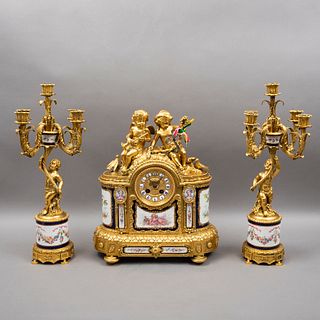 GUARNICIÓN. FRANCIA, CA. 1900. Estilo NAPOLEÓN III. Consta de reloj y par de candelabros, bronce dorado y porcelana. 47 y 55 cm de alt.