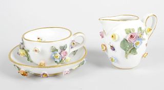 A Meissen miniature porcelain teacup and saucer, each with a white glazed ground hand painted and wi