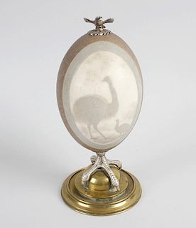 A 19th century carved emu egg, the paneled decoration depicting an emu with chick, mounted upon a cl