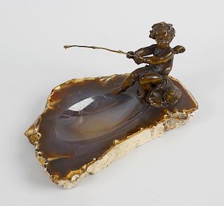 A late 19th century bronze study of a cherub, seated upon a rock, and fishing above a dished agate b