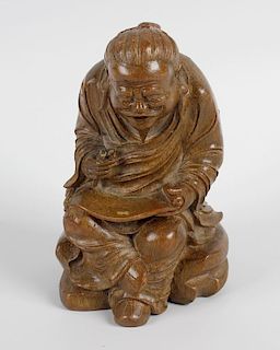 An oriental carved bamboo figure, modelled as a seated elder, cross legged with a scroll across his