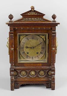 An oak cased mantel clock, the carved case of architectural form, its sides with fitted brass lion m