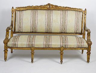 A French giltwood open arm settee. The acanthus leaf carved back and flower head supports leading to