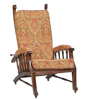 American Victorian Carved Oak Morris Chair, c. 1900, the adjustable back with two lions' head finials, with upholstered arms, on reeded legs on paw fe