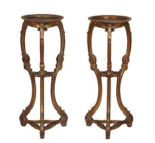 Pair of Carved Giltwood Pedestals, 21st c., the circular top with a relief leaf border, on tripodal legs joined by a center pierced stretcher and a lo