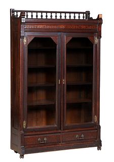 American Carved and Incised Walnut Bookcase, c. 1890, spindled back gallery over a front geometric frieze above double glazed doors, and two lower dra