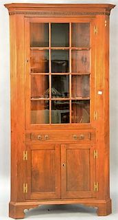 Cherry custom made corner cabinet having one glass door over one drawer over double bottom doors, top having cut shell shaped shel...