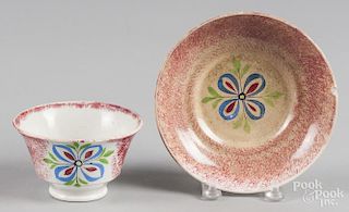 Red spatter cup and saucer with a four-petal flower decoration.