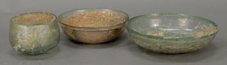 Three Roman glass dishes/bowls including pale green glass and iridescent glass with heavy incrustation, 2nd - 5th century A.D. dia. ...