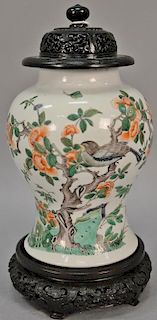 Chinese Kangxi porcelain jar having painted bird and butterflies on blossoming tree with carved hardwood cover resting on carved har...