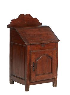 French Provincial Carved Walnut Slant Top Desk, 19th c., the rectangular top arched back splash over a lifting lid and a fielded panel cupboard door, 