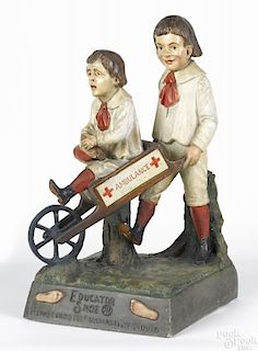Plaster advertisement for Educator Shoe, featuring a boy pushing another in an Ambulance