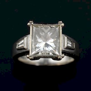 Princess cut diamond ring, weighing 3.41 carats,  in a bezel setting with a tapered baguette to each shoulder. Mounted in whi