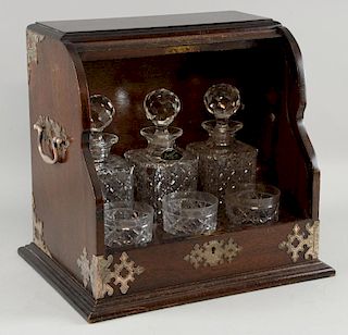Early 20th century oak fronted tantalus with three decanters and three tumblers.