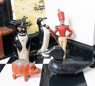 Two Painted Cast Iron Penguin Form Door Stops, a Band Leader, and a Red Piggy Bank