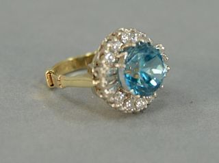 Gold ring set with large round with light blue topaz surrounded by diamonds.