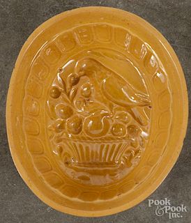 Yellowware food mold with a parrot perched on a basket of fruit, 3 1/4'' h., 8'' w., 7'' d.