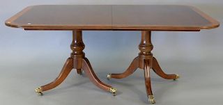 Henredon mahogany dining table with banded inlaid top set on double pedestal base with brass capped paw feet having two 24" l