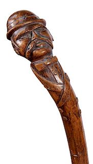 319. Folk-Art Man Cane – Ca. 1880 – A carved one-piece burl with a gentleman atop in a boiler hat/handlebar mustache, bow