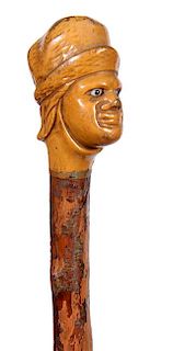 379. Gentleman Folk-Art Cane – Ca. 1900 – A carved portrait cane of a gentleman with two colored glass eyes and a cap. Or