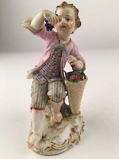Meissen figurine of a young boy sitting on rocks with a sickle and a basket of g
