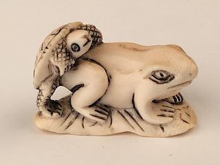 A carved Netsuke figure of a turtle climing on a frog.