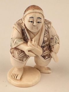A carved Netsuke figure of a man standing with his tools.