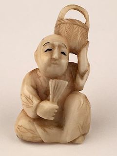 A carved Netsuke figure of a seated man holding a basket overhead.