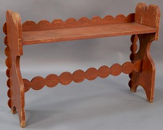 Red painted bucket bench having scallop carved back and support, on shelf on boot jack ends.  ht. 31in., wd. 45in., dp. 11 3/