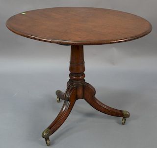 Mahogany tip table on turned shaft set on three downswept members ending in brass feet with wheels, early 19th century. 
ht. 