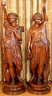 Pair of carved walnut Classical female figures clad in draped clothing, arm raised holding a chalice, each holding a cup, eac