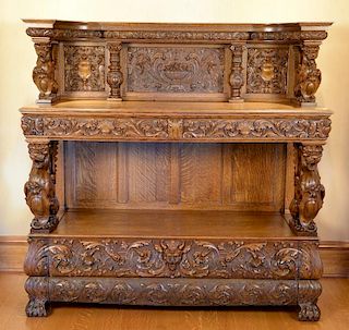 Oak server having carved panel back with curved compote of fruit supported by winged griffins over two drawers over wing grif