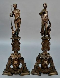 Pair of bronze fireplace chenets, topped with partially clad female and male set on figural base with winged female and male