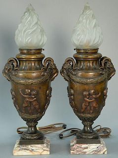 Pair of bronze torchere form table lamps with frosted flame form shades over bronze urn body with ram's head handles and mold