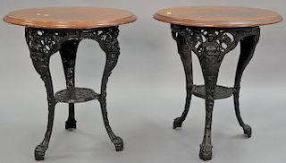 Pair of oak top cafe tables with iron base having female figures and paw feet, ht. 28in., dia. 26in. Provenance: Property fro