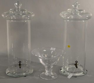 Three piece lot including pair of large cylinder crystal urns having covers and spigots (ht. 22in.) along with a crystal comp