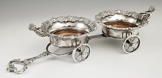 Silverplate Figural Wine Trolley, 20th c., with two coasters with foliate rims mounted with a cherub, around turned hardwood 