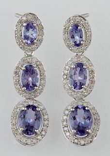 Pair of 14K White Gold Pendant Earrings, each with a stud with an oval tanzanite atop a border of round diamonds, suspending 