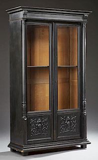 French Ebonized Carved Walnut Bookcase, c. 1870, the stepped crown over double setback doors with glazed upper panels and low