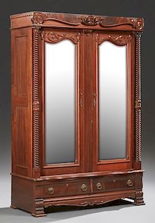 American Late Victorian Mahogany Armoire, c. 1900, with a floral carved crest over double wide arched beveled mirror doors fl