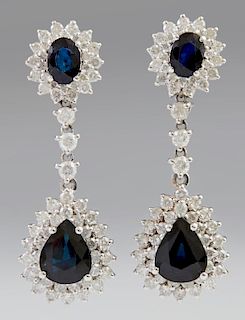 Pair of 14K White Gold Pendant Earrings, each stud with an oval blue sapphire atop a conforming diamond mounted border, suspe