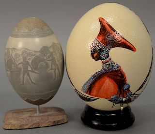 Two ostrich eggs to include a carved Scrimshaw ostrich egg depicting primitive figures with huts and weapons, and a Carol Smit Eggar...