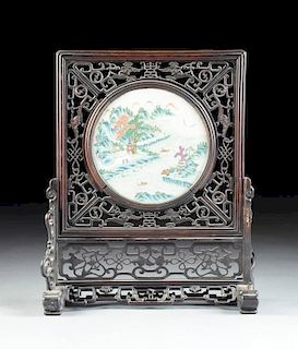 A CHINESE LATE QING DYNASTY/EARLY REPUBLIC PERIOD CARVED ROSEWOOD TABLE SCREEN MOUNTED WITH A CIRCULAR FAMILLE VERTE PORCELAIN PLAQUE, PROBABLY JINGDE