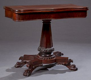 American Carved Mahogany Games Table, 19th c., the serpentine top over a wide skirt, on a tapered octagonal support to a tripodal base on large paw fe