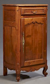 French Provincial Carved Cherry Confiturier, early 20th c., the rounded edge and corner top over a frieze drawer and a cupboard door with a brass escu