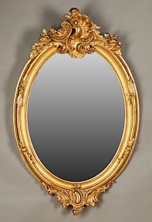 Louis XV Style Gilt and Gesso Overmantle Mirror, early 20th c., the elaborate pierced scroll and floral crest over an oval wide beveled plate within a